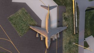 A large four-engine military jet with USAF markings is parked on a ramp next to grass and taxiway lines.