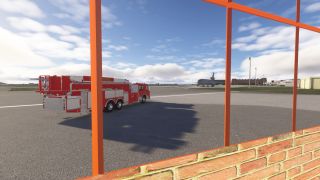 A red airport fire truck is parked on the tarmac near a large military jet, viewed through an orange-framed window.