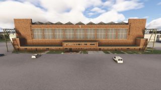 A large brick hangar with a number 1 above its windows faces a mostly empty parking area with three parked vehicles.