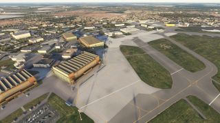 Several large hangars and parked aircraft are visible near taxiways and ramps, with a town and fields in the background.