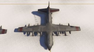A large four-engine military transport aircraft with dark camouflage and red wingtips is parked on a snowy apron viewed from above.