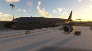 A dark gray U.S. Air Force jet with a tiger emblem is parked on the ramp at sunset beside a ground power unit.