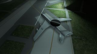 A military aircraft with a large radar dome is parked on a taxiway at night under overhead lights, surrounded by grass.