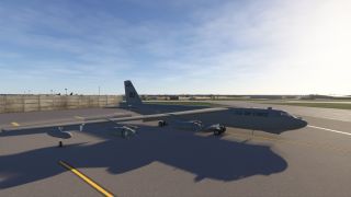 A U.S. Air Force jet with four engines is parked on a ramp near a concrete barrier under a clear sky.