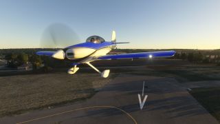 A blue-and-white single-engine aircraft flies low over a marked runway, with fixed landing gear and two occupants visible beneath its canopy.