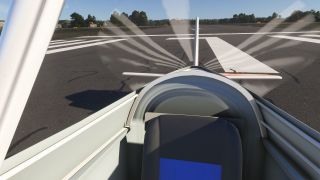 A rearward cockpit view shows a dark seatback, white tail surfaces with red stripes, and runway markings beneath a clear sky.