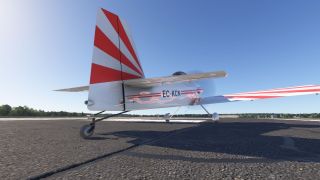 A red-and-white tailwheel aircraft marked EC-KCN stands on pavement, viewed from behind with its striped tail prominent against clear blue sky.