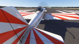 A red-and-white propeller aircraft marked EC-KCN sits on a runway, viewed from behind with a pilot visible beneath its bubble canopy.