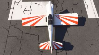 A white aircraft with red sunburst wing and tail stripes sits on cracked runway pavement, viewed directly from above.