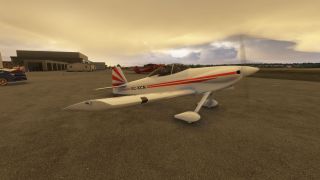 A white low-wing aircraft with red stripes and a spinning propeller sits on the apron near hangars under a golden sky.