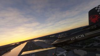 A black aircraft marked EC-KCN banks above a waterfront runway at sunset, displaying a red bull emblem and checkered tail markings.