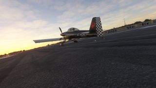A black single-engine aircraft with a checkered tail and EC-KCN registration sits on airport pavement beneath a yellow-tinged sky.