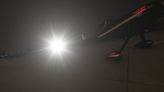 A black RV-4 with white stripes and red graphics sits on pavement at night, its bright wing light producing glare.