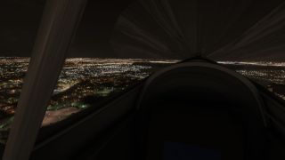 A dark cockpit with a curved instrument coaming and prominent left support overlooks illuminated streets and buildings at night.