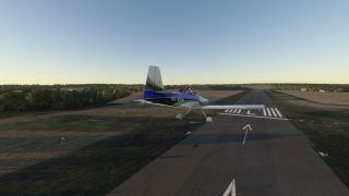 A blue-and-white light aircraft flies just above a marked runway threshold, with fixed landing gear and surrounding fields visible.