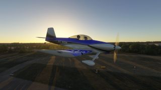 A blue-and-white propeller aircraft flies low over an airfield, with two occupants beneath its bubble canopy and long shadows below.