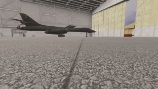 A dark gray B-1 bomber sits inside a steel-framed hangar with landing gear extended and maintenance scaffolding near its tail.