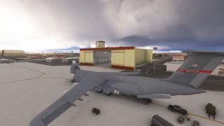 A gray U.S. Air Force C-5 Galaxy sits outside an open hangar, with cargo ramps lowered and ground vehicles nearby.