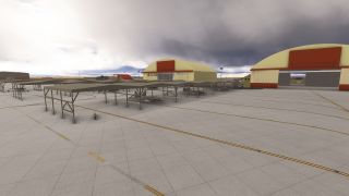 Military helicopters sit beneath open-sided shelters on a marked apron beside yellow hangars with red trim under dark clouds.