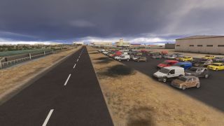 Rows of cars and vans fill a parking lot beside a large hangar and straight access road under dark clouds.