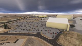 Large pale-yellow hangars border crowded parking lots and aircraft aprons at a desert airport beneath dark clouds.