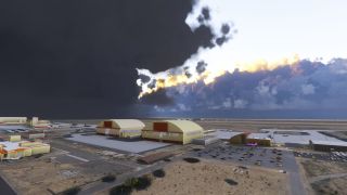 Two large arched hangars stand beside airport aprons and a car park beneath dark clouds with sunlit edges.
