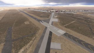 Runway 23R extends across a dry airfield, with connecting taxiways, hangars, and distant mountains beneath low clouds.