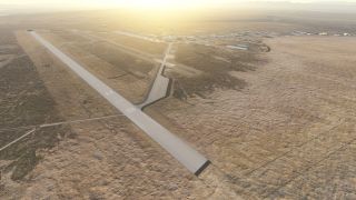 A paved runway and connecting taxiways cross dry terrain, with airport buildings beyond and distant mountains under low sunlight.