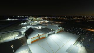 Floodlit hangars with orange trim border marked aprons and crowded parking lots, while blue taxiway lights outline the airport at night.