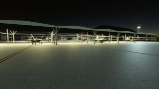 Several gray fighter jets sit beneath open-sided shelters on a floodlit apron at night, with yellow taxi lines crossing the foreground.