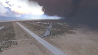 A long runway and connecting taxiways cross dry terrain, with airport buildings beneath contrasting bright and dark clouds.