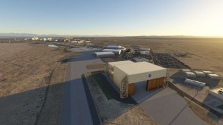A NASA-marked hangar stands beside taxiways and parking lots at a desert airfield, with distant mountains and long shadows.