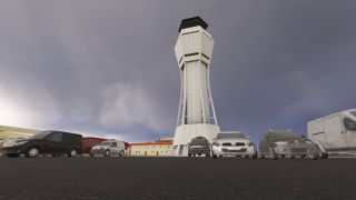 A tall white control tower rises behind parked cars and vans, with low airport buildings beneath a gray, cloudy sky.