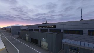 Ålesund Airport’s gray terminal displays illuminated Vigra signage beside apron markings, with snowy hills beneath a cloudy pink sky.