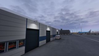 An airport service building with blue garage doors borders an apron with parked airliners, service vans, and illuminated light poles.