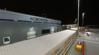 Ålesund Airport’s terminal stands under floodlights at night, with covered walkways, red barriers, and a service vehicle beside the apron.