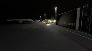 An Airbus airliner sits on a floodlit apron at night beside a large hangar, with a helipad marking in the foreground.