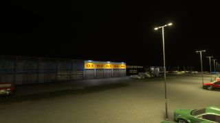 Tall streetlights illuminate parked cars outside a DHL building with numbered garage doors at night.