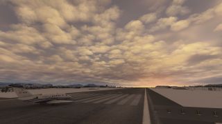 A white business jet sits beside runway threshold markings, surrounded by snow-covered terrain beneath golden clouds.
