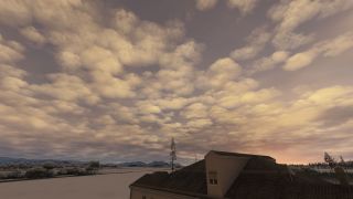 Golden clouds fill the sky above a tiled roof, snow-covered fields, scattered trees, and distant hills.
