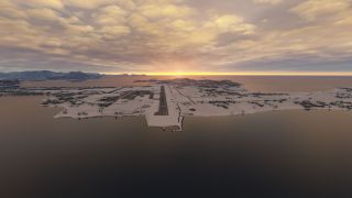 A runway extends across a snow-covered coastal airport, with apron buildings, surrounding water, and distant mountains beneath orange-lit clouds.