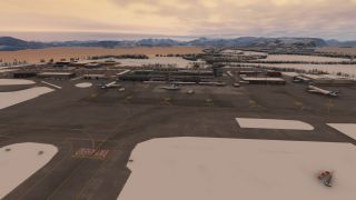 Three airliners sit outside an airport terminal beside snow-covered taxiways, with water and mountains stretching beneath an orange sky.