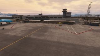 A KLM aircraft sits beside an airport terminal and control tower, with ground vehicles on the apron and snow-covered mountains beyond.