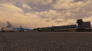 A KLM airliner sits beside service vehicles outside an airport terminal, with a control tower beneath an orange, cloud-filled sky.
