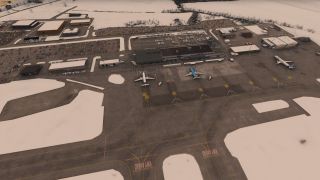 Three airliners sit on marked apron stands beside an airport terminal, with snow-covered grounds and busy car parks behind it.