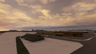 Snow surrounds a dark pitched-roof building and ochre airport hangars, with a distant control tower beneath golden clouds.