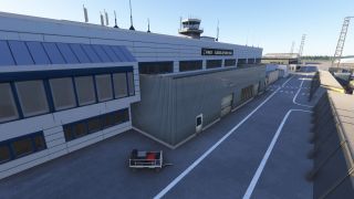 Ålesund Airport’s terminal displays blue-framed windows and rooftop antennas, with a control tower above and a baggage cart beside marked service lanes.