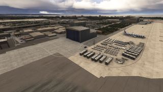 A blue-and-white striped airliner sits beside hangars and rows of airport buses, baggage carts, and mobile stairs on a coastal apron.