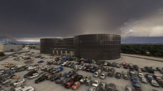 Rows of parked cars fill a lot outside a dark glass building with rounded wings beneath heavy gray clouds.