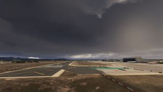 Dark clouds hang over an airport runway and intersecting taxiways, with parked airliners beside a large hangar on the right.
